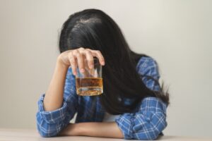 A young woman with long black hair covers her face while holding an alcoholic drink and wondering: Can a DUI prevent you from being a legal guardian or conservator?